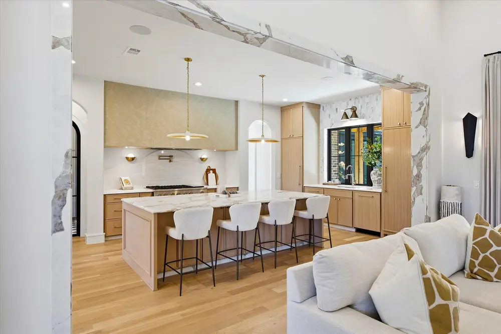 Open kitchen with a white oak island, brass pendants and a marble backsplash