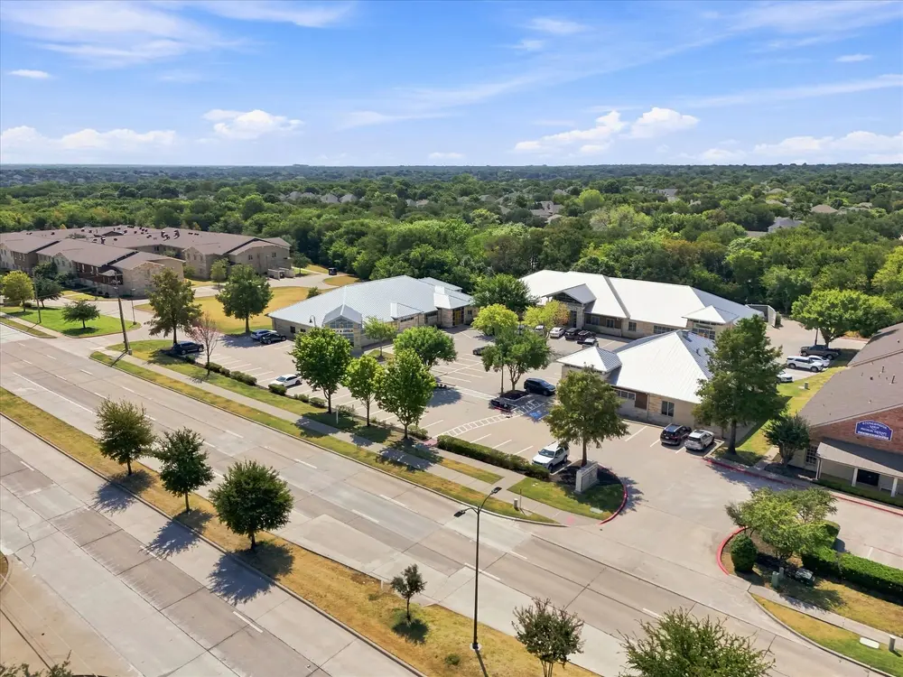 Aerial of office buildings set back from a divided parkway, with tree cover and neighborhoods beyond